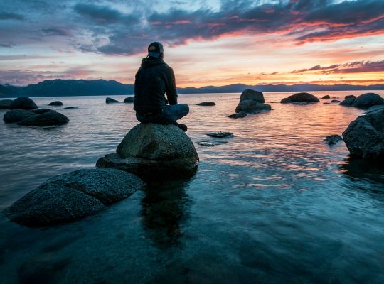 man sitting on rock surrounded by water