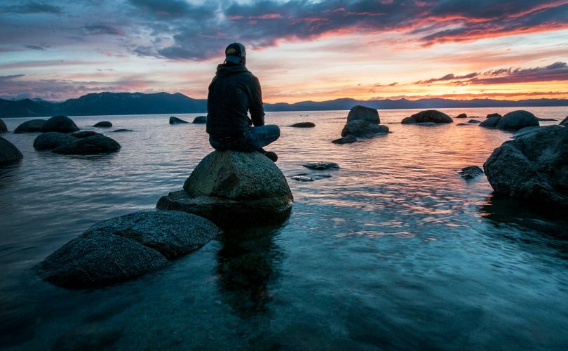 man sitting on rock surrounded by water