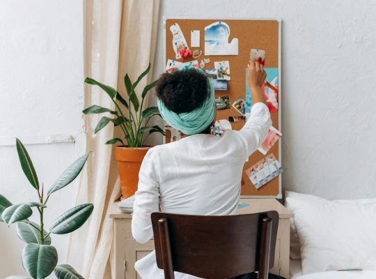 A woman in a cozy room organizing a vision board with photos and ideas.