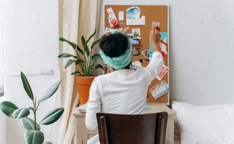 A woman in a cozy room organizing a vision board with photos and ideas.