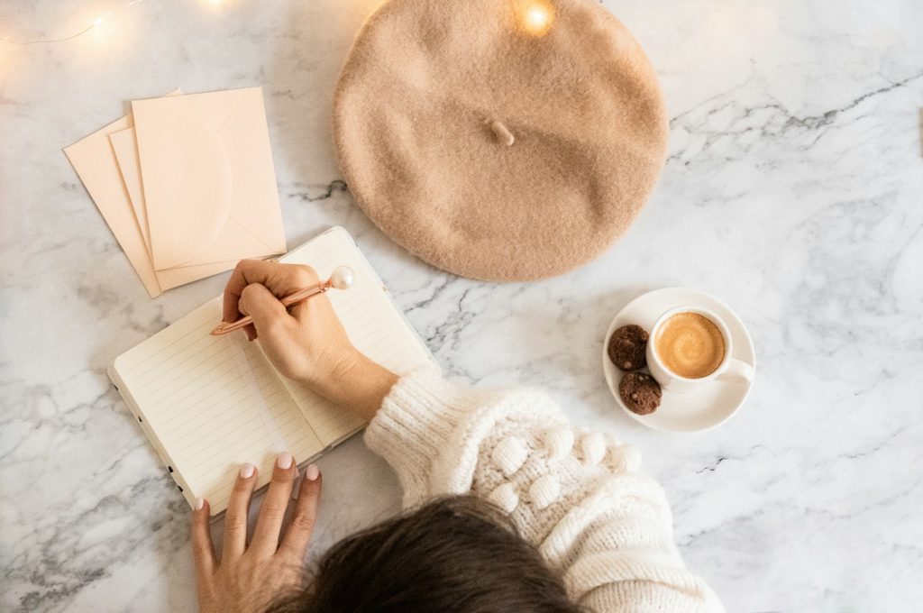 a person writing on a notebook next to a cup of coffee