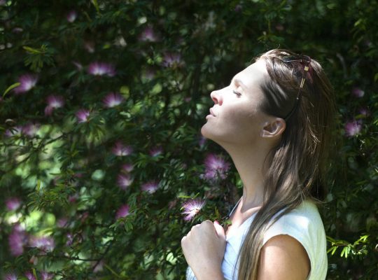 A woman enjoying a serene moment in a sunlit garden, surrounded by vibrant flowers.