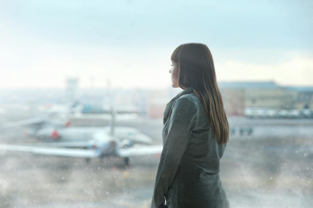 A woman gazing at airplanes through a window at Kyiv's airport terminal, capturing a moment of reflection.
