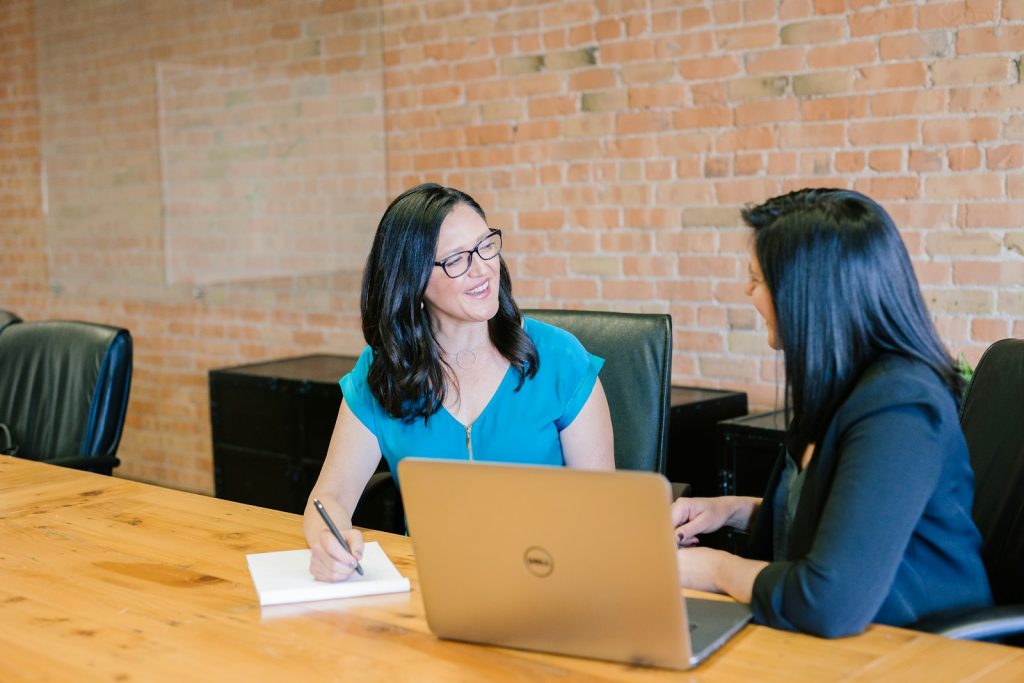 woman in teal t-shirt sitting beside woman in suit jacket Photo by Amy Hirsch